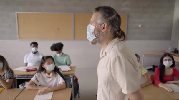 Maestra caucásica en máscara protectora enseñando a un grupo multiétnico de estudiantes durante la pandemia covid-19. — Vídeos de Stock