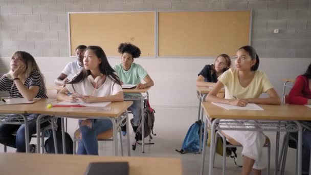 Dans la salle de classe du secondaire : Un enseignant enthousiaste marche parmi des rangées d'enfants brillants et diversifiés et explique la leçon. Groupe de jeunes intelligents et multiethniques apprenant. — Video