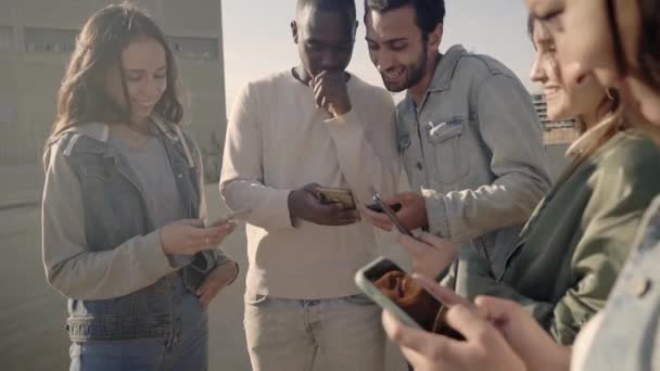 Movimiento lento de un grupo de amigos usando sus teléfonos celulares riendo y divirtiéndose al aire libre. Jóvenes del milenio conectados en las redes sociales. — Vídeos de Stock