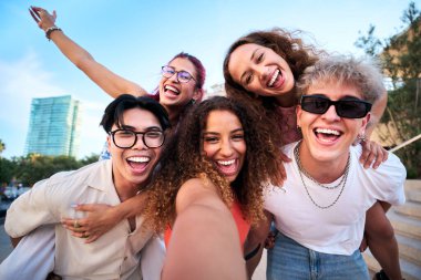 Beş neşeli arkadaş eğleniyor, neşeli bir kentte, neşeli bir selfie için poz veriyor, kahkaha ve enerjiyi paylaşıyorlar. Çeşitli genç yetişkinler seyahat havasından ve dışarıdaki gerçek bağlantıdan zevk alıyorlar..