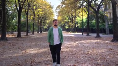 Sıradan bir adam, bir sonbahar günü ağaç sıralı şehir caddesinde yürüyor, yeşil bir gömlekle gülümsüyor ve rahatlıyor. Sıcak yapraklı şehir yaşam tarzı, yumuşak ışık ve açık derinlik perspektifi.