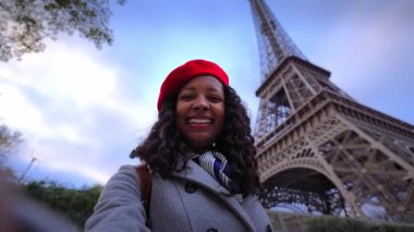 Afrika milenyumu, mavi saatte Paris 'teki Eyfel Kulesi' nin yanında selfie çekerken kameraya gülümsüyor. Kırmızı bir bere ve palto takıyor, kent seyahati titreşimlerini doğrudan gözleriyle yakalıyor..