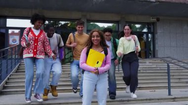 Dersten sonra bir araya gelen mutlu bir grup öğrenci üniversite kampüsündeki derslerin bitişini kutlayan kameraya bakıp gülümsüyor ve topluluk ve arkadaşlığın tadını çıkarıyor.