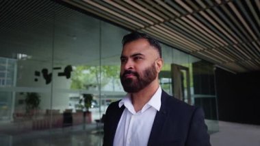 Hintli bir profesyonelin modern bir ofis koridorunda yürürken, odaklanmış, kararlı bir ifade koridoru iş yeri atmosferi ve ileri hareketi ile yan tarafa bakarken görüntüsü..