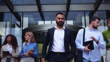 Çeşitli iş arkadaşları modern cam bir ofisten ayrılıp sabah işe gidip gelirken girişten geçiyorlar. Günlük iş tarzı, konuşma ve hareket takım çalışması öneriyor.