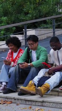 Dikey. Çeşitli öğrenciler dersten sonra kampüs basamaklarında oturup sohbet ederken ve notları kontrol ederken akıllı telefonlara dalıyorlar. Teknolojik kullanım, eğitim materyalleri ve gevşek bir mola ile gündelik üniversite havası.