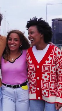 Dikey. Çeşitli çok kültürlü genç bin yıllık arkadaşlar şehir palmiyeleri boyunca kucaklaşıyorlar. Üniversiteliler kampüse giderken gülerek dışarı çıkıyorlar. Neşeli öğrenciler birlikte.