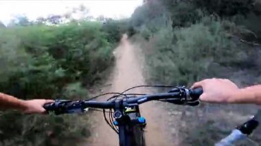 Yeşil ormanın ortasında, tek bir toprak yolda hızla giden, dağ bisikleti süren, tanınmayan yetişkin bir adamın görüntüsü. Dışarıda aşırı riskli sporlar yapan genç bir bisikletçinin gidonunun arkasındaki bakış açısı