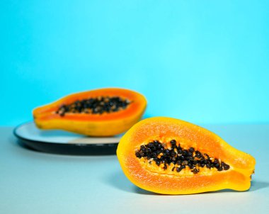 Mavi Arkaplanda Yeşil ve Tohumlu Papaya 'nın İki Yarısı, Minimalizm Eğilimli Gıda, Sağlıklı ve Detokslu Yeme, Çiğ Öğle Yemeği, Copyspace, Diyet ve Yararlı Yemek, Egzotik Yemek