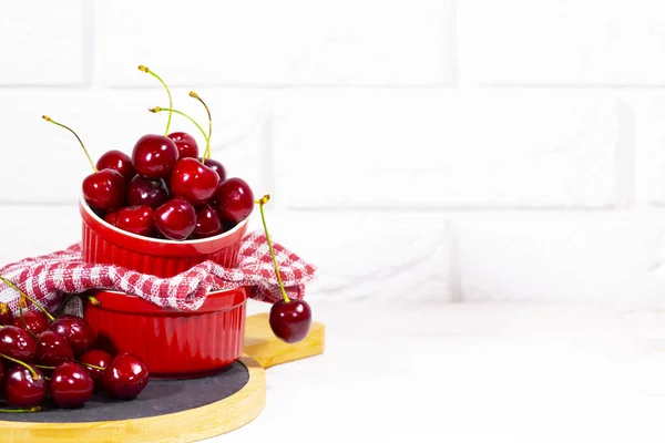 Sweet Cherry v Red Bowls na dřevěném stole na bílém cihlovém pozadí. Vitamínové jídlo. Kopírovat mezeru — Stock fotografie