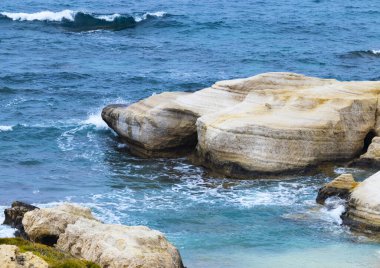 Okyanus dalgaları sahile taşlı arka planda sıçrar, denizdeki uçurumlar, Kıbrıs 'ın en tepedeki havadan görünüşü, okyanusun altın kumla kaplı olduğu doğa arka planı.