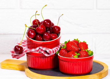 Beyaz tuğlalı arka planda, ahşap masadaki kırmızı kasedeki sulu taze çilekler. Vitamin yiyeceği. Uzayı kopyala Vejetaryenlik