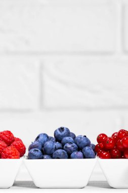 Beyaz arka planda beyaz seramik kasede taze çiğ çilekler. Mesaj için yer var. Frenk üzümü, ahududu ve yabanmersini