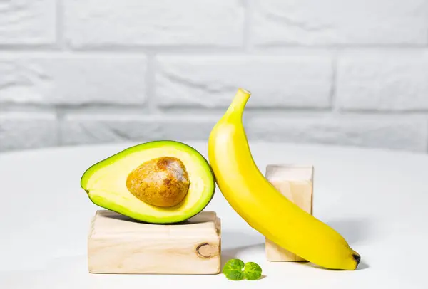 Kreativ avokado, banan och mikro grön balans trä står och podium., vit bakgrund, Jämvikt hälsosam mat. Balanserat näringsbegrepp — Stockfoto