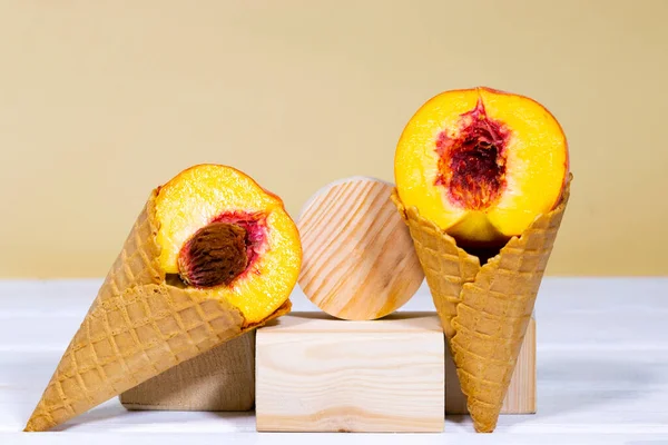 Half a ripe peach in sweet wafer cone on wooden stands over light orange background. Healthy nutrition, seasonal harvest of fruits. Copy space, Equilibrium floating food balance