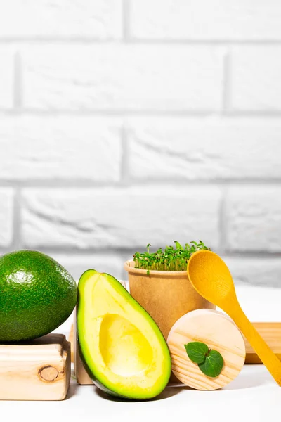 Kreativt stilleben med avokado, mikrogrön och sked på vit bakgrund med trästativ och podium. Jämvikt hälsosam mat. Balanserat näringsbegrepp. — Stockfoto