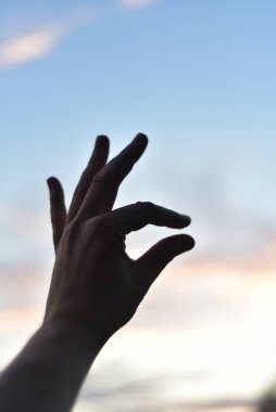 Beyaz bulutlu mavi gökyüzünün arka planına karşı bir el, işaret ve başparmak birbirine yakındır, yani bu hareketle - çok değil, biraz.