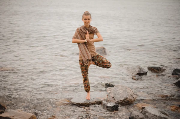 Kvinnan gör yoga tree pose namaste på stenen nära havet — Stockfoto