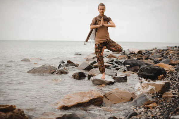 Kvinnan gör yoga tree pose namaste på stenen nära havet — Stockfoto