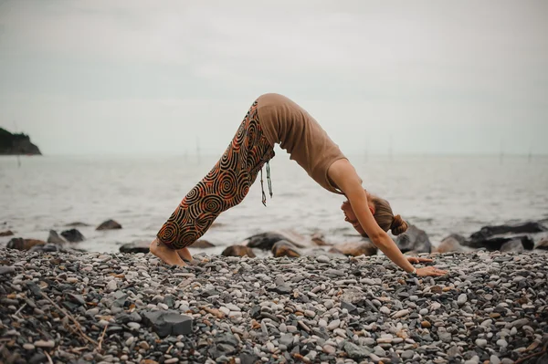 Jonge vrouw beoefenen van yoga in neerwaartse facing hond pose op strand — Stockfoto