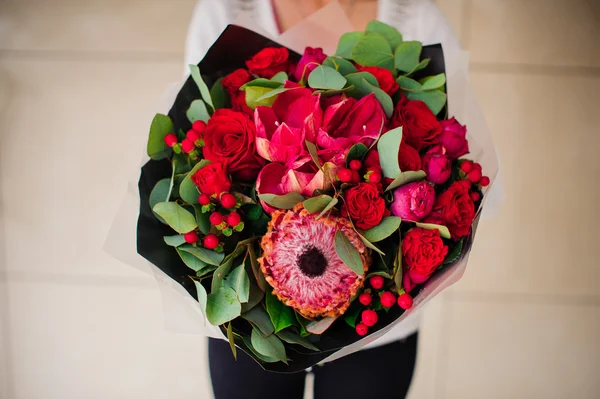 Beau bouquet de différentes fleurs rouges avec du papier noir dans les mains — Photo