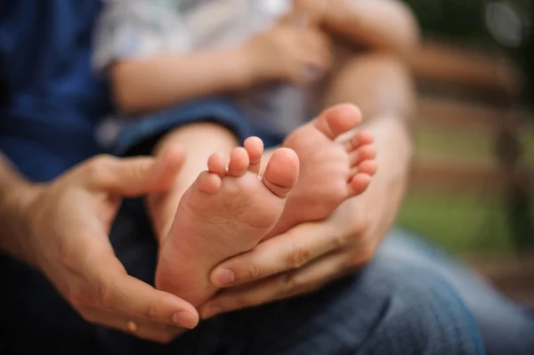 Petits pieds de bébé en papas mains sur la nature à l'extérieur. parc d'été en arrière-plan . — Photo