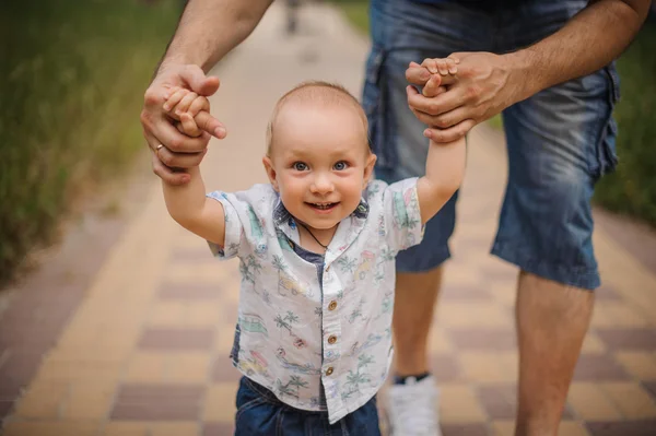 Babyjongen leren om te lopen en het maken van zijn eerste stappen bedrijf handen van vader. — Stockfoto