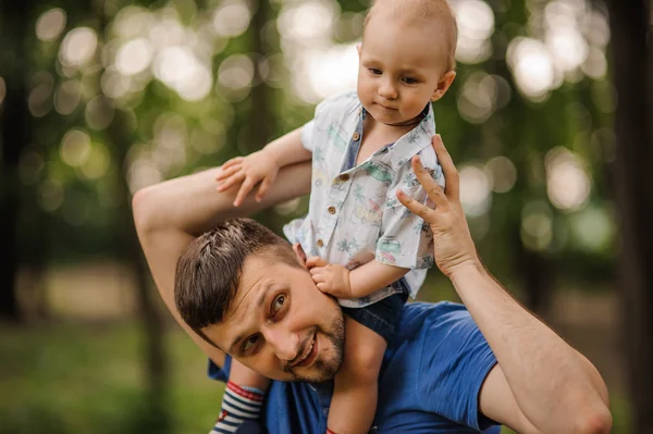 Vrolijke kleine zoon op schouders bij de papa in de zomertuin — Stockfoto