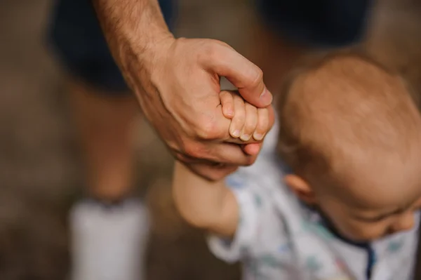 Babyjongen leren om te lopen en het maken van zijn eerste stappen bedrijf handen van vader. — Stockfoto