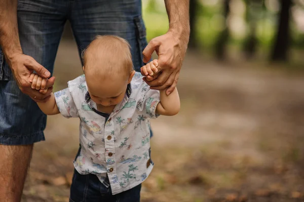 Babyjongen leren om te lopen en het maken van zijn eerste stappen bedrijf handen van vader. — Stockfoto