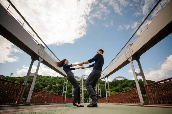 Bonito feliz jovem casal de homem e mulher girando ao ar livre na ponte — Fotografia de Stock