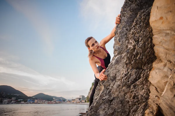 Portrait of young female rock climber overhanging cliff. Beautiful blue sky, city mountains on the background. — Stock Photo, Image