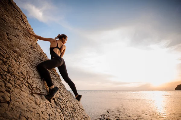 Vrouwelijke extreme klimmer verovert steile rots tegen de zonsondergang over de rivier. — Stockfoto