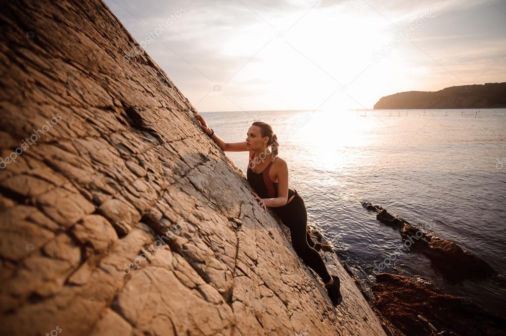 Female extreme climber conquers steep rock against the sunset over river.
