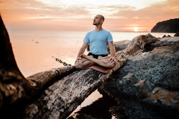 Man mediterar på brutna träd nära havet solnedgång. Gör yoga utomhus — Stockfoto