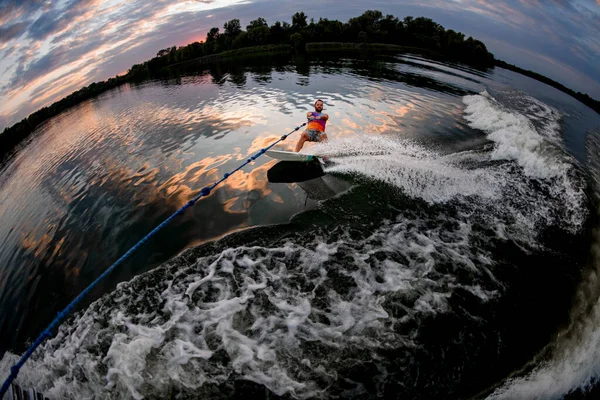 Vista del hombre sosteniendo la cuerda y el wakeboard de montar a caballo en la onda de la lancha —  Fotos de Stock