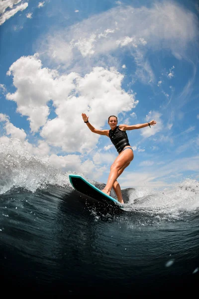 Atractiva mujer cabalgando en la tabla despierta surfeando en el río contra el cielo nublado — Foto de Stock