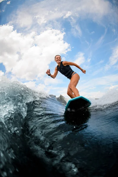 Спортсменка і активна мокра жінка їде хвилею на дошці для серфінгу проти хмарного неба — стокове фото