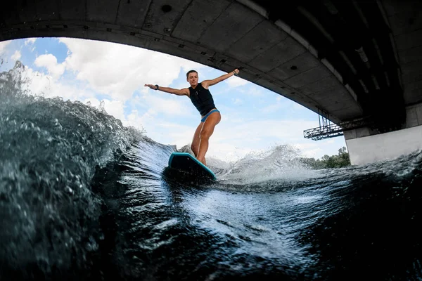 Ung våt kvinna i svart badväst rider nerför floden vågen på wake board — Stockfoto