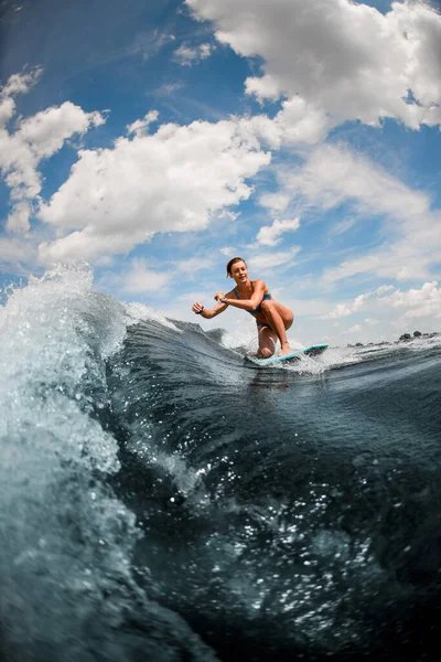 Sportliche Frau reitet auf Welle und sitzt auf Surfbrett vor blauem Himmel — Stockfoto