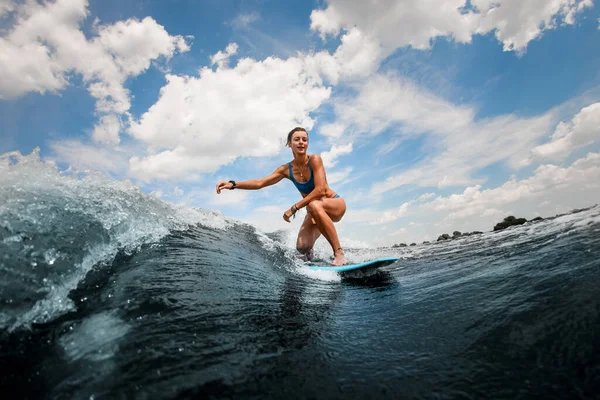 Femme athlétique et active chevauchant sur la vague assise sur une planche de surf contre le ciel bleu — Photo