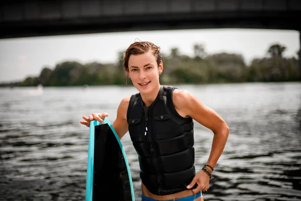 Joven mujer deportiva se para con tabla de surf sobre fondo borroso — Foto de Stock