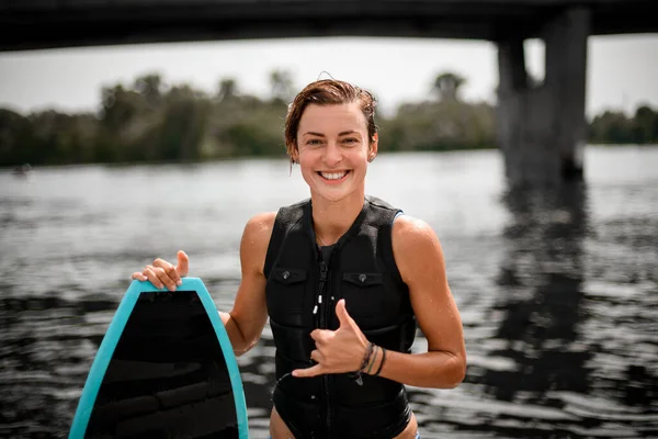 Mujer feliz se para con tabla de surf y muestra gesto de la mano. — Foto de Stock