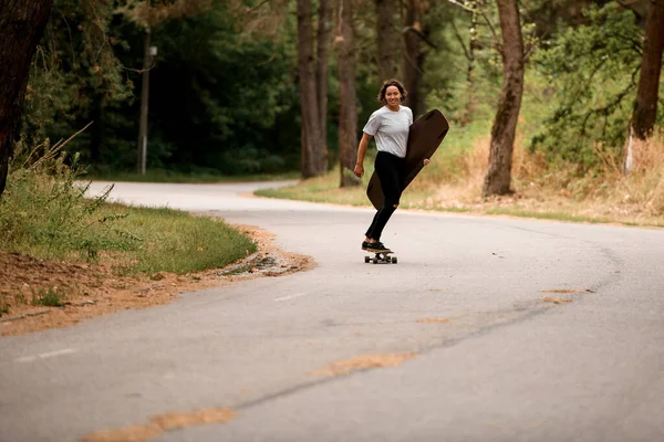 Gelukkig lachende vrouw rijdt op skateboard met wakeboard in haar hand — Stockfoto