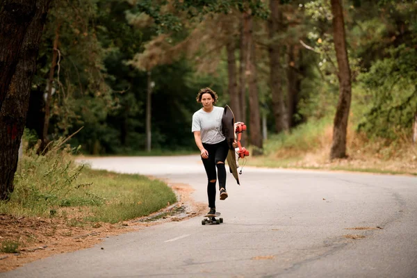 Νεαρή γυναίκα με wakeboard στο χέρι είναι skateboarding γρήγορα στο δρόμο — Φωτογραφία Αρχείου