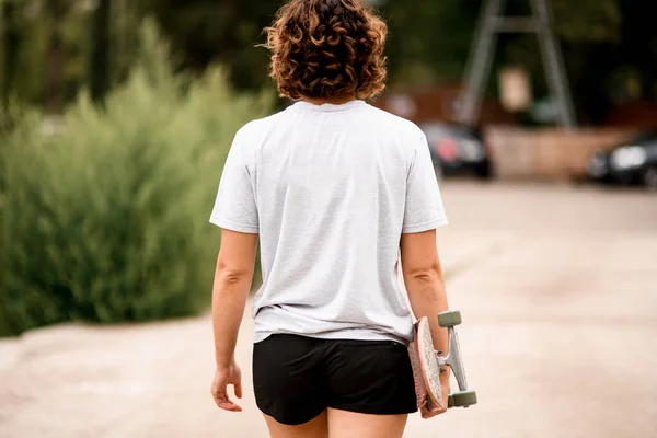 Visão traseira da bela jovem mulher em branco t-shirt segurando skate — Fotografia de Stock