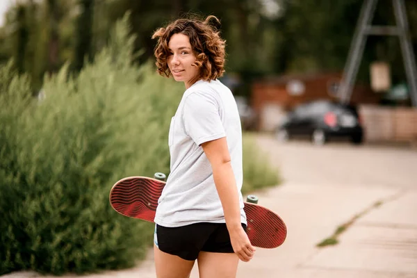 Šťastná žena v bílém tričku s hlavou otočenou zpět a skateboard v ruce — Stock fotografie