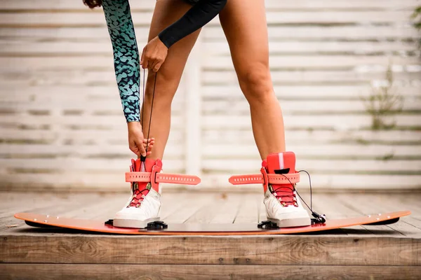 Uitzicht op de benen van sportieve vrouw die laarzen van wakeboarding board binden. — Stockfoto