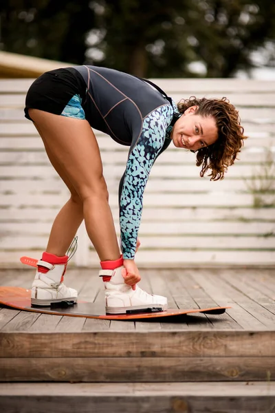 Jonge vrouw fix haar benen in laarzen op een wakeboarding board — Stockfoto