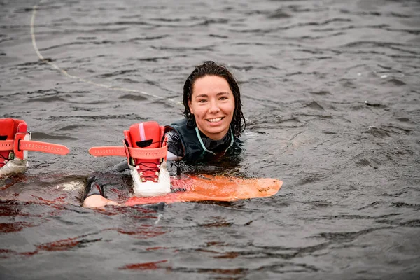 Sonriente joven mujer nada en el agua en chaleco con wakeboard brillante —  Fotos de Stock